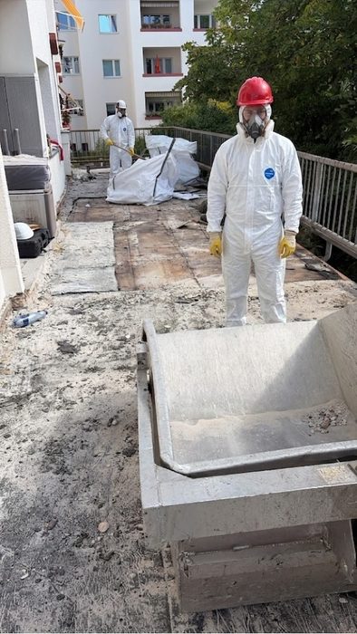 Mitarbeiter in Vollschutz mit Atemschutzmaske vor der Abwurfmulde